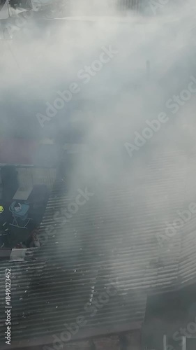 A fire in a private residential area: thick white smoke rises from the roofs of private homes. Aerial (drone) view of the scene. Fire rescue operations: on the charred roof, the remains of the fire.