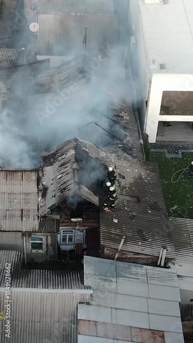 A fire in a private residential area: thick white smoke rises from the roofs of private homes. Aerial (drone) view of the scene. Fire rescue operations: on the charred roof, the remains of the fire.