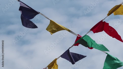 Colorful flags flutter in the sky during a festival at a local park in the afternoon sunlight with clouds in the background