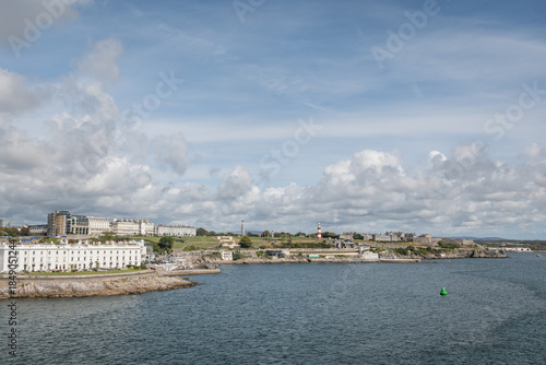  coastal view of Plymouth coastline city tourist attraction lighthouse beacon and other town buildings on the sea front.