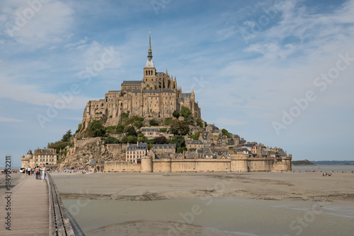 tidal island Mont Saint-Michel in Normandy France unesco historic coastal landmark with grassy dry land field in foreground below the fortified structure. Monestary abbey is popular tourist attraction