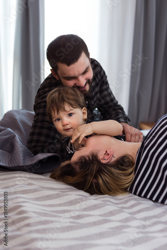 Young parents in bedroom playing with infant son in family bed