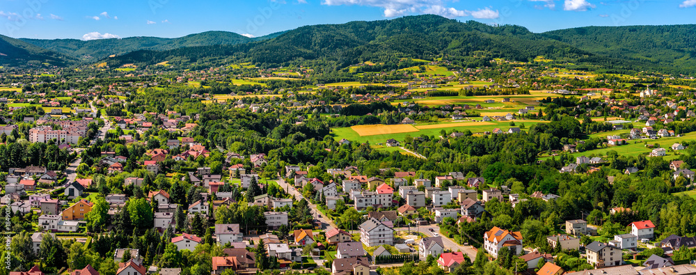 Fototapeta premium Aerial panoramic view of disperse housing of residential district of Andrychow city along railway track with Beskidy Mountains in background in Lesser Poland