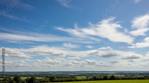 Vast expanse of rolling green fields under a dynamic sky with wispy clouds