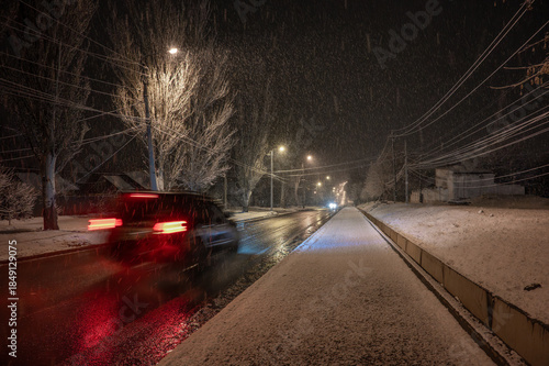 Winter cityscape with snowfall and car on road in motion