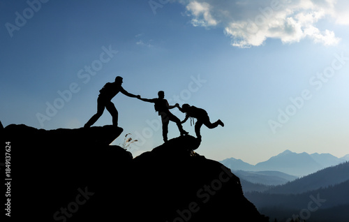 Silhouette of hikers helping each other climb a mountain peak at sunset, teamwork and collaboration concept.