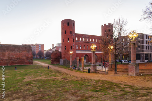 Turin, Italy. View from the Palatine Towers Archaeological Park of Porta Palatina, the ancient Roman gate of Turin, with brick towers, arches, walls, and open green space at dusk. 