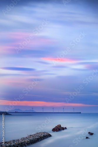 Long exposure sunset at Arrigunaga beach with offshore wind turbines and colorful purple clouds