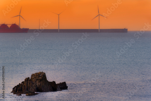 Sunset at Arrigunaga beach with wind turbines under orange sky Renewable energy concept at dusk
