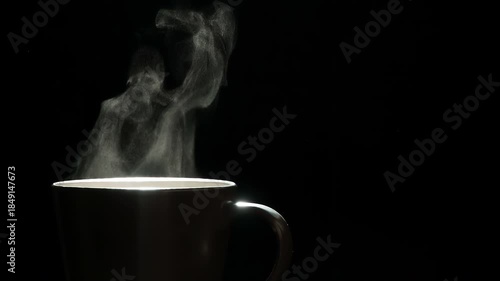 Mug of Hot Coffee. A trickle of steam rises and twists gracefully from a cup of hot Coffee. Backlight illuminates brown cup on a black background