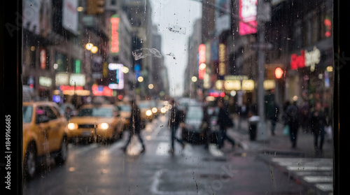 A rain-drenched view of a New York City street. Pedestrians cross at a crosswalk, and yellow cabs glow through the wet glass of the window.