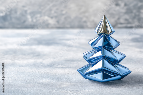Decorative blue Christmas tree ornament with a shiny silver top, placed on a textured gray surface, creating a festive and modern holiday atmosphere with copy space