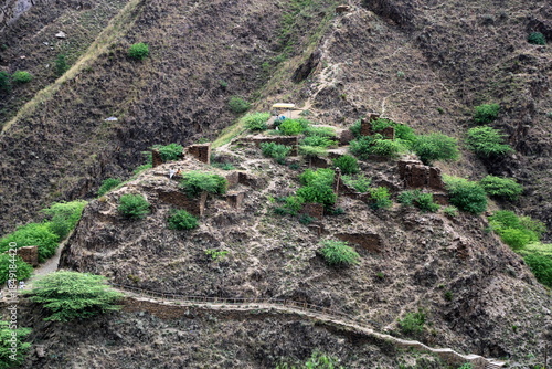 View of ancient ruins scattered among rugged, arid hillsides, dotted with tenacious green shrubs under a muted sky, Takht Bhai, Khyber Pakhtunkhwa, Pakistan.