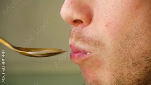 Profile close up young unshaven man mouth eating traditional olivier salad, also known as potato salad, bringing golden spoon to his lips, chewing food contentedly. Man eating olivier