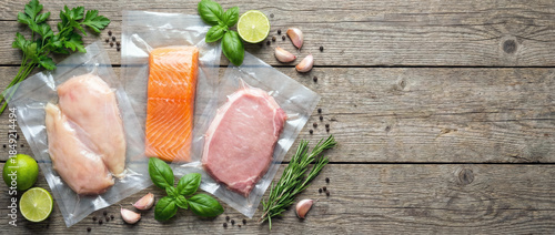 Vacuum-sealed bags with raw chicken, salmon, and veal on rustic wooden table with herbs