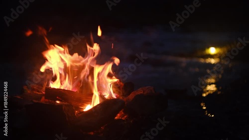 Night relaxing campfire and mountain river in light of flashlight. Cozy bonfire, burning old wood. Camping vibes and outdoor lifestyle mood