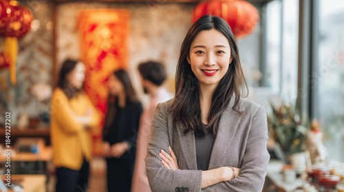 Confident professional with colleagues: A confident young Asian professional stands poised, arms crossed, exuding leadership as her colleagues converse softly in the background.  Lunar new year