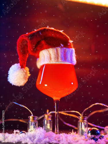 Stylish glass of craft beer in Santa's Christmas hat on a snowy bright background