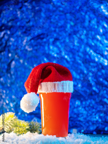 Craft beer glass in Santa's Christmas knitted hat on a snowy blue background, copy space