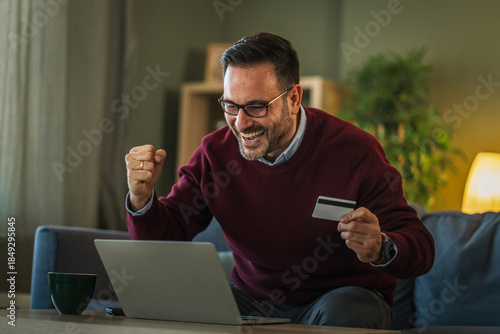 Fotografia Man celebrating online shopping success with credit card