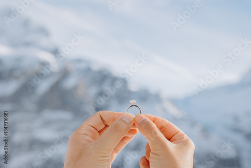 Romantic marriage proposal in the Swiss Alps, close-up of hands with a sparkling diamond ring.
