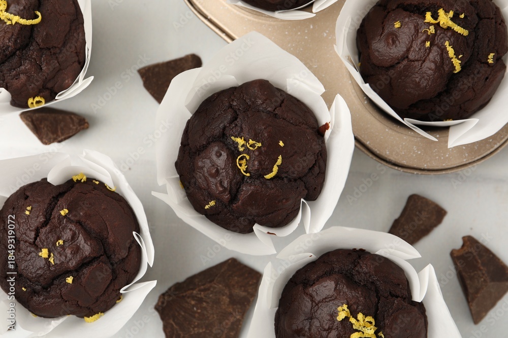 Naklejka premium Tasty chocolate muffins with lemon zest on white table, flat lay