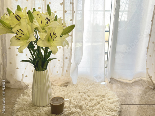White Lilies in a Vase on beige carpet Near Sunlit Window. Morning cup of coffee.