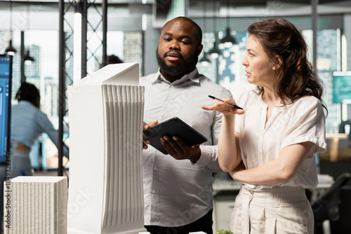 Diverse urban development experts review architectural 3D models and city planning proposals, ensuring infrastructure growth forecasts for sustainable housing construction master plan.