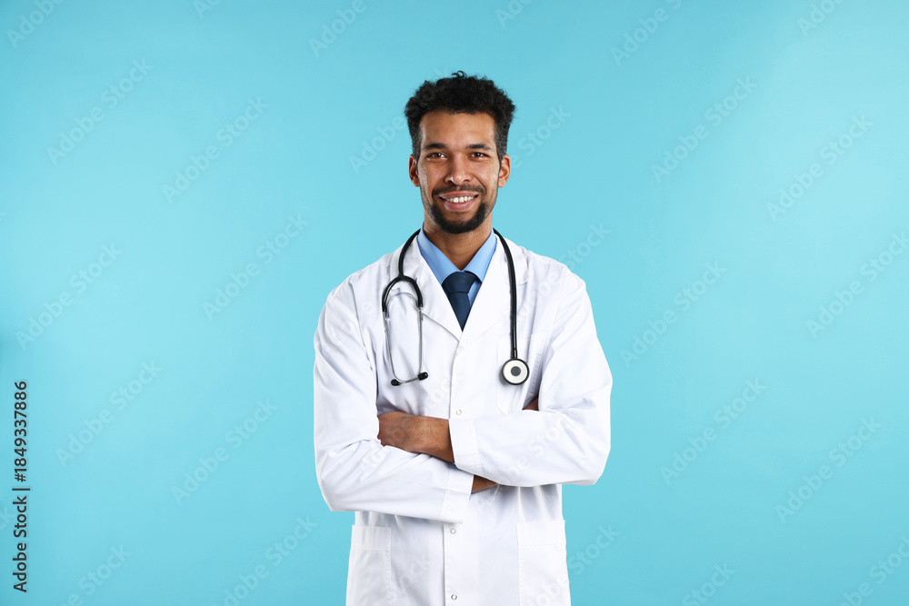 Fototapeta premium Smiling doctor in medical uniform with stethoscope on light blue background