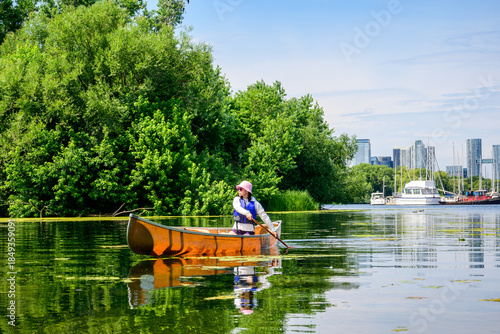 Foto A woman paddles a canoe across still water near a marina on the Toronto Islands, combining summer recreation with scenic waterfront views and relaxed outdoor leisure