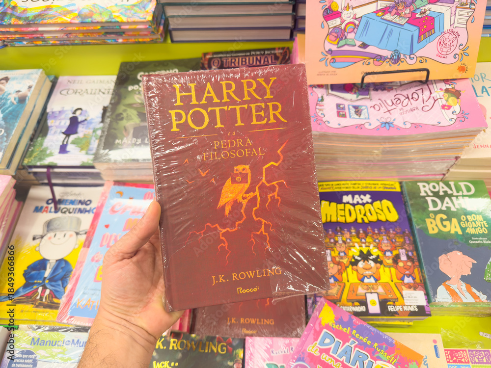 Naklejka premium BELO HORIZONTE, MG, BRAZIL, DECEMBER 12, 2025 A new, plastic-wrapped edition of Harry Potter and the Philosopher's Stone is held in hand at a vibrant bookstore.