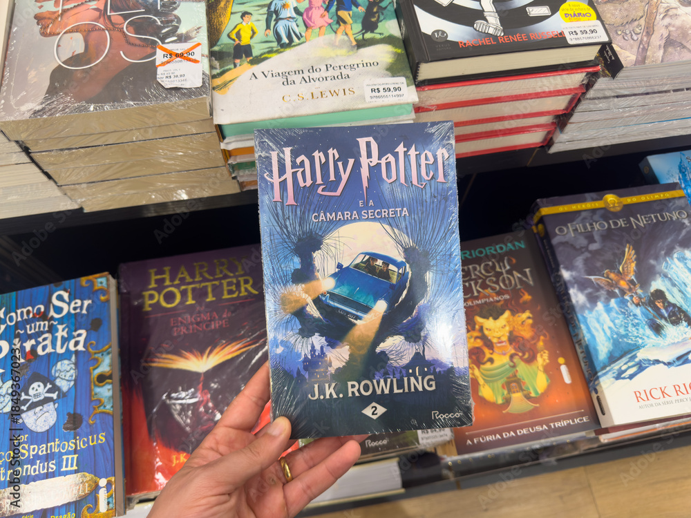 Obraz premium BELO HORIZONTE, MG, BRAZIL, DECEMBER 12, 2025 A hand holds the iconic 'Harry Potter and the Chamber of Secrets' book in a vibrant bookstore setting, celebrating the magic of reading.