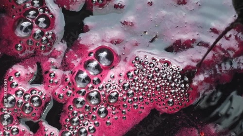 Bubbling foam moves on grape burgundy juice into a pan during the winemaking process.