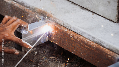 Extreme danger close-up of a worker's bare hand holding a metal tube during arc welding with bright sparks. Concept of severe industrial safety negligence, lack of PPE, and high risk of injury.
