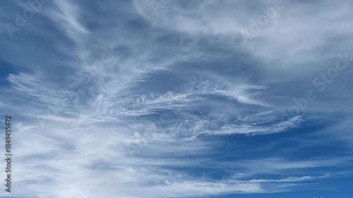The video captures a serene expanse of deep blue sky, featuring delicate, feathery white clouds gracefully drifting across the frame. These high-altitude formations, likely cirrus, create a calming an