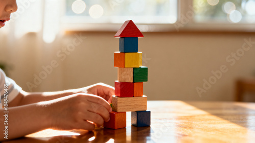 Close up of kids hands stacking multicolored wooden blocks into tower on polished desk in cozy home setting