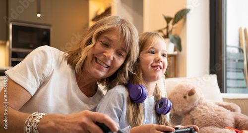 Portrait of happy grandmother and granddaughter playing together with video game controllers on a couch