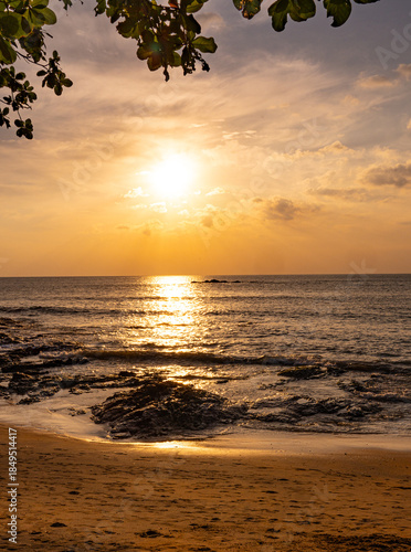 Dramatic sunset with sun reflection on a rocky beach in Khao Lak Thailand. Golden light illuminates the rocks, sea and sky, capturing a tranquil tropical coastal landscape at dusk.