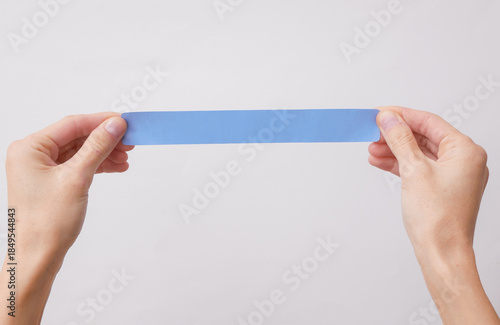 Hand holding a paper bracelet or blue sticker on a white background