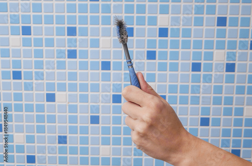 Hand holds old, used toothbrush in the bathroom