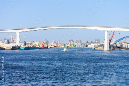 Namihaya Bridge Arching Over Osaka Bay Port with Cargo Ships and Industrial Cranes in Japan. A scenic view of the Namihaya Bridge spanning the industrial harbor of Osaka.