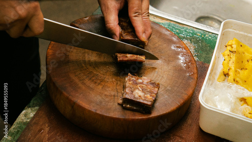 Hands cutting cooked pork on wooden chopping board