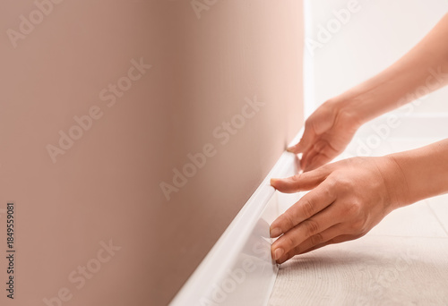 Photography Female hands installing white plinth on brown wall in room, closeup
