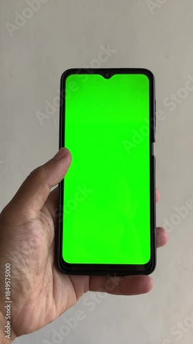 Hand holding smartphone with green screen mockup and thumb touching display