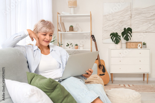 Mature woman using laptop on sofa at home