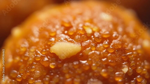 Macro of fresh laddu surface, grainy texture glowing with ghee, tiny almond fragments embedded, warm orange tones, gentle handheld movement.