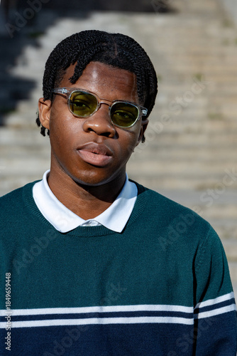 Portrait of a stylish black man wearing sunglasses and green striped sweater standing in a urban setting