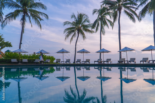 Beautiful sunrise sky with palm trees by seaside pool reflecting water, luxury tropical resort atmosphere
