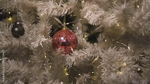 A close-up of a decorated Christmas tree with a shiny red disco ball ornament and black ornaments among white branches.