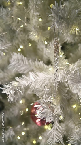 A close-up view of a white Christmas tree with soft, fluffy branches and colorful ornaments. Warm lights create a cozy atmosphere.
